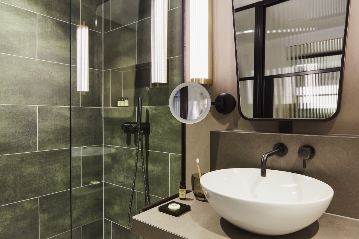 Bathroom in Hotel Indigo, London featuring Viero UK Marmorin Hydro in grey on the walls behind the sink, with green tiles in the shower, creating a mo