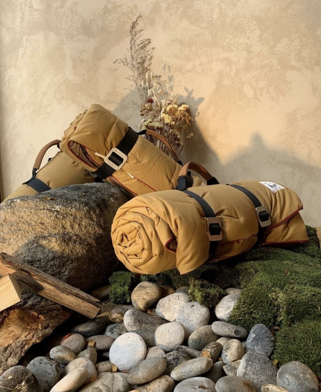 Close-up of rolled outdoor gear and sleeping mats staged against a textured Viero Ghibli wall finish, with natural elements like river stones, moss, a