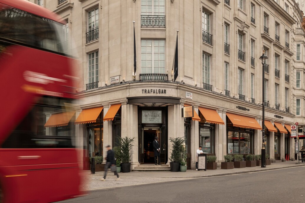 Exterior view of The Trafalgar St. James hotel in central London with a red double-decker bus passing on the left